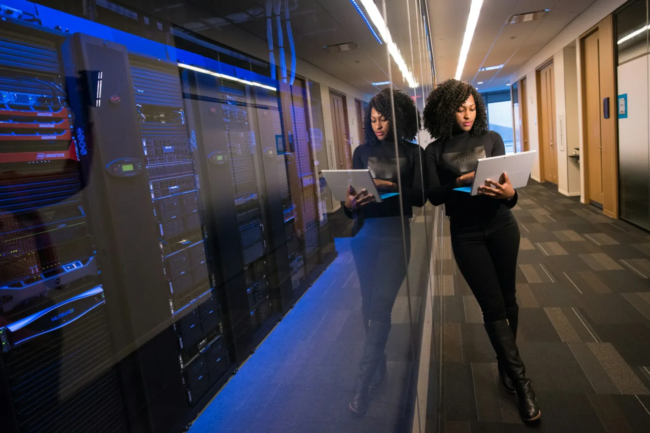 An IT technician with a laptop in a server room corridor
