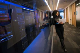 A woman with a laptop in a server room corridor